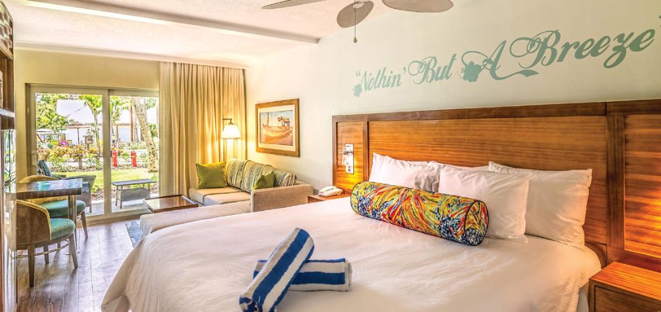 "Nothin' But A Breeze" written on the wall above a resort bed with a wood headboard in a Margaritaville Vacation Club suite.