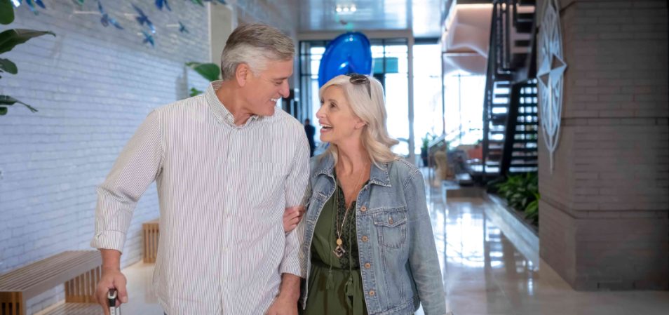 Smiling older man and woman walking through the lobby of a Margaritaville Vacation Club resort.
