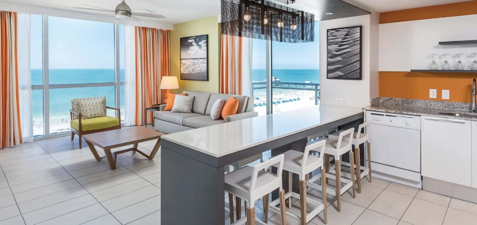 A modern living room and kitchen in a Margaritaville Vacation Club suite with a view of the ocean.